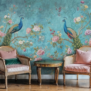 May include: Two vintage-style chairs with pink cushions and green throw pillows are placed in front of a teal blue wall with a floral and peacock design. A small round wooden table sits between the chairs.