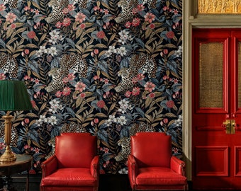 May include: Two red leather chairs with gold accents sit in front of a wall with a dark floral wallpaper featuring leopards and gold accents. A green lamp with a gold base sits on a table in front of the chairs. A red double door with gold accents is in the background.