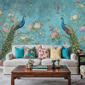 May include: A white sofa with teal, floral, and yellow throw pillows sits in front of a teal wall with a floral and peacock design. A wooden coffee table with a book and a vase of flowers sits in front of the sofa.