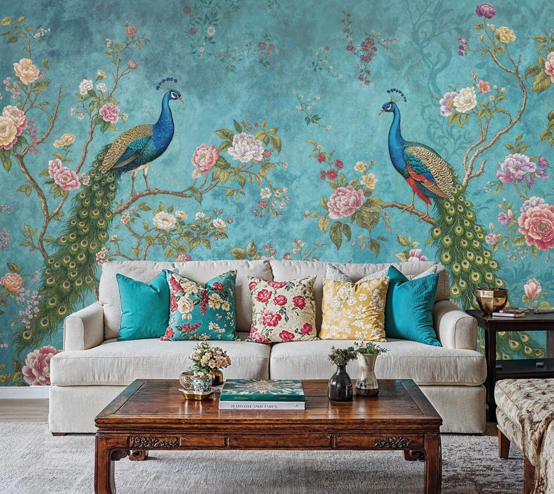 May include: A white sofa with teal, floral, and yellow throw pillows sits in front of a teal wall with a floral and peacock design. A wooden coffee table with a book and a vase of flowers sits in front of the sofa.