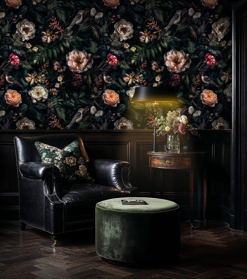 May include: A black leather armchair with a floral patterned cushion sits in front of a dark floral wallpaper. A green velvet ottoman sits in front of the chair. A table lamp with a black shade illuminates the scene.