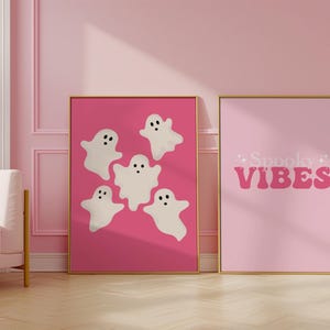 May include: Two pink framed prints with a Halloween theme. One print features five white ghosts on a pink background. The other print has the text "Spooky Vibes" in pink letters on a pink background.