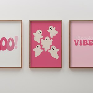 May include: Three framed prints with a pink background. The left print has the word "BOO!" in pink letters. The center print has five white ghosts with black eyes on a pink background. The right print has the words "Spooky Vibes" in pink letters.