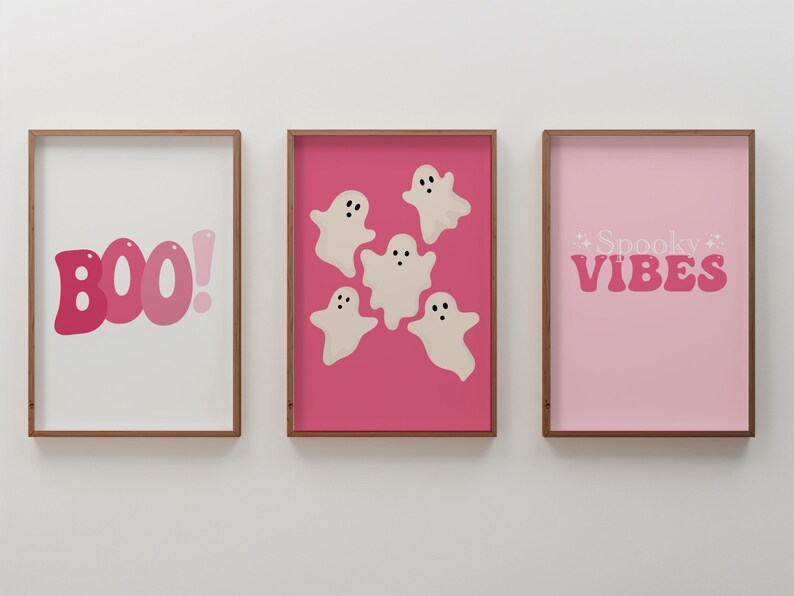 May include: Three framed prints with a pink background. The left print has the word "BOO!" in pink letters. The center print has five white ghosts with black eyes on a pink background. The right print has the words "Spooky Vibes" in pink letters.