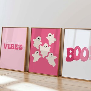 May include: Three framed prints with a pink background. The left print says "Spooky Vibes" in pink letters. The middle print has five white ghosts with black eyes on a pink background. The right print says "BOO!" in pink letters.