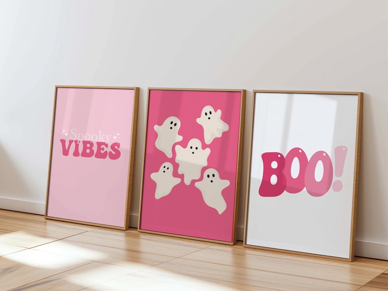 May include: Three framed prints with a pink background. The left print says "Spooky Vibes" in pink letters. The middle print has five white ghosts with black eyes on a pink background. The right print says "BOO!" in pink letters.
