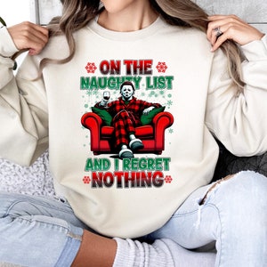 Könnte beinhalten: Ein weißer Pullover mit einem weihnachtlichen Motiv, das eine Figur in einem rot-schwarzen karierten Hemd zeigt, die in einem roten Sessel sitzt. Der Text auf dem Pullover lautet "On the Naughty List and I Regret Nothing".