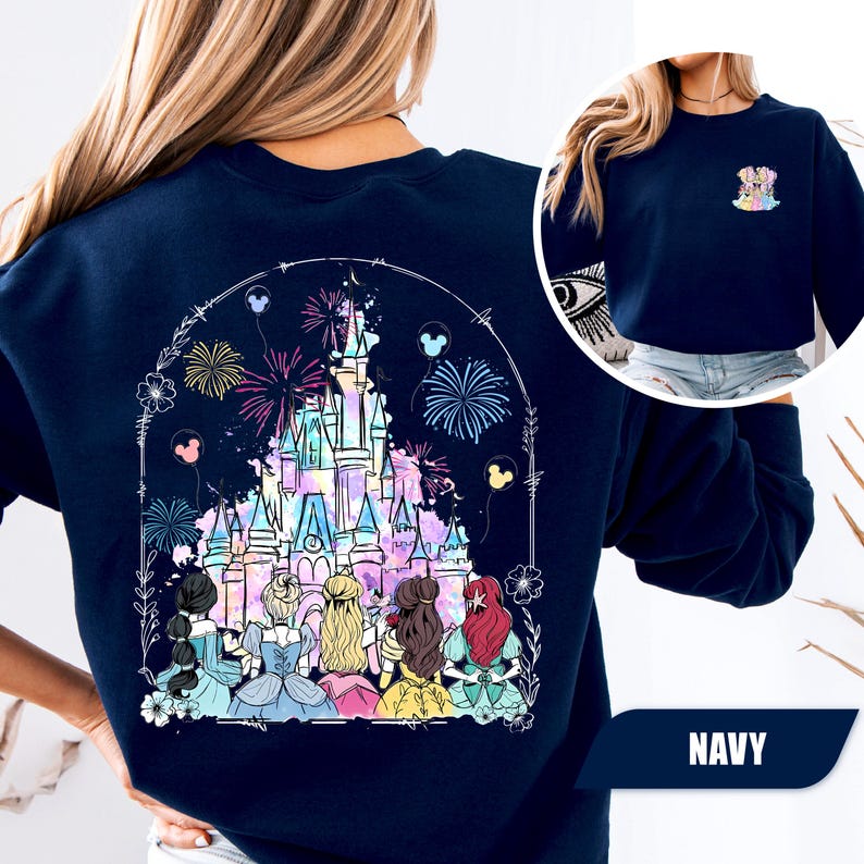 May include: Navy blue sweatshirt featuring a colorful illustration of a fairytale castle with fireworks and Disney princesses. The design is framed by a floral arch and Mickey Mouse balloons. A smaller image of the design is on the upper right.