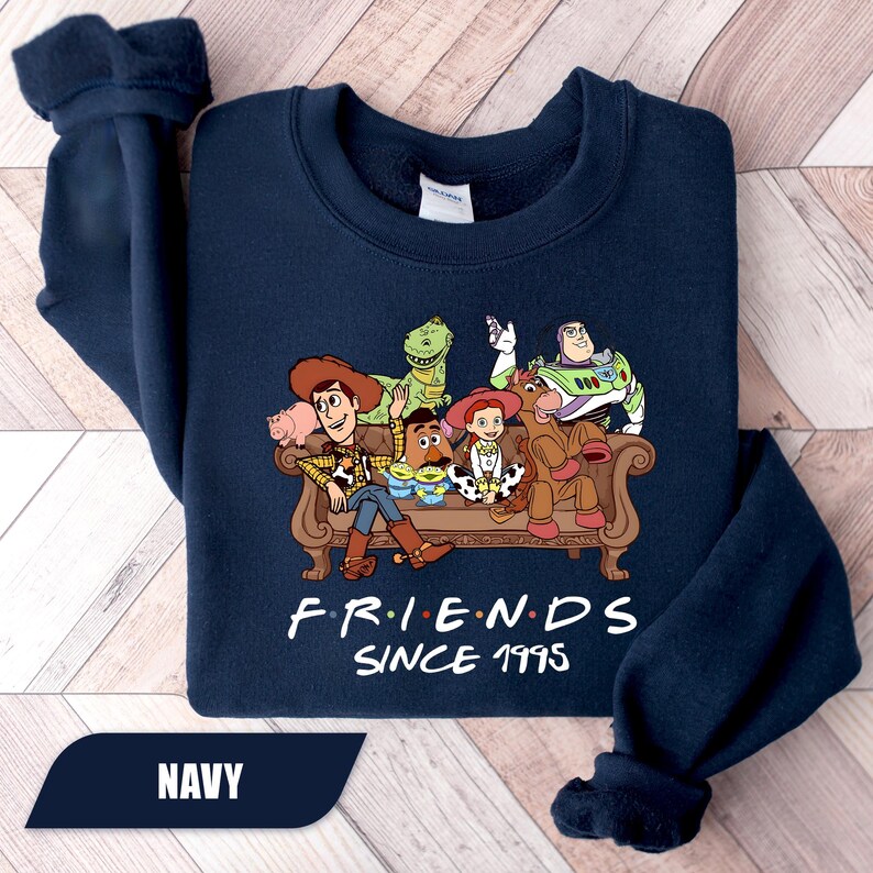 May include: Navy blue sweatshirt featuring a graphic of characters from the movie Toy Story. The characters are seated on a brown couch. The text "FRIENDS SINCE 1995" is printed below the graphic.