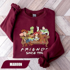 May include: Maroon sweatshirt featuring a graphic of Toy Story characters sitting on a couch. The text "FRIENDS SINCE 1995" is printed below the graphic. The word "MAROON" is displayed in a banner at the bottom.