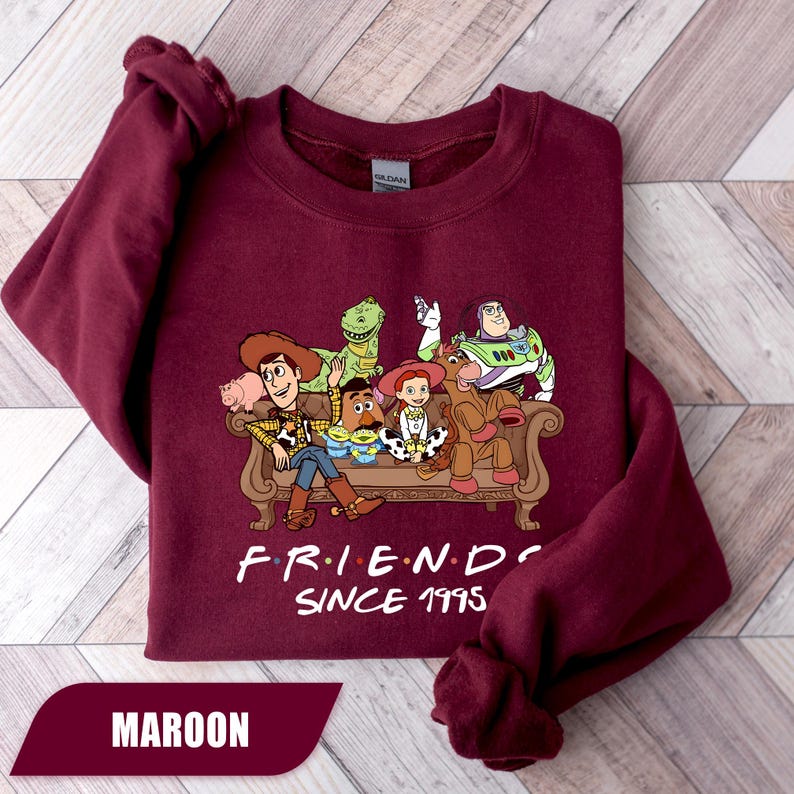 May include: Maroon sweatshirt featuring a graphic of Toy Story characters sitting on a couch. The text "FRIENDS SINCE 1995" is printed below the graphic. The word "MAROON" is displayed in a banner at the bottom.