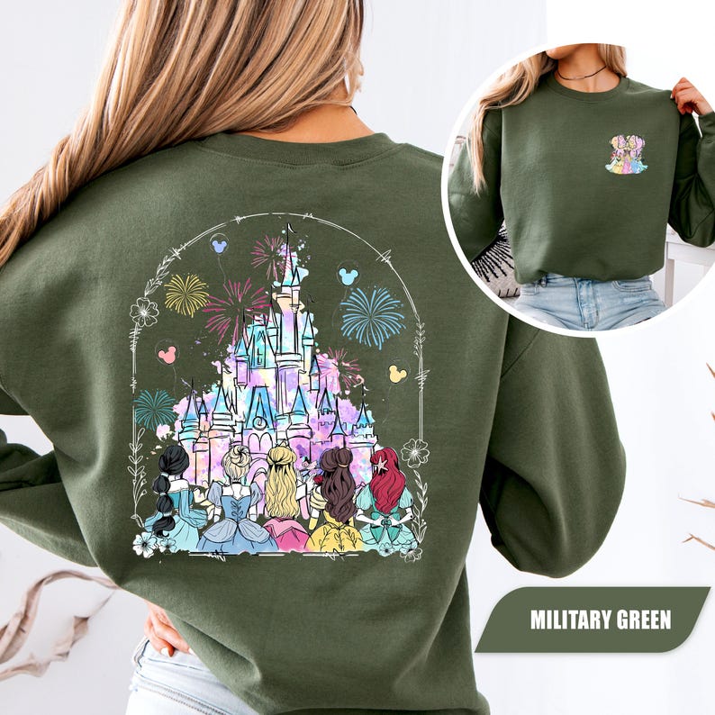 May include: Military green sweatshirt featuring a colorful graphic of a castle, fireworks, and cartoon characters. The design is framed by a floral and dotted border. A smaller graphic of a dog is on the front. The text "MILITARY GREEN" is at the bottom.