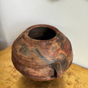 Puede incluir: Una maceta grande de terracota marrón con una abertura ancha y dos asas pequeñas. La maceta tiene un aspecto rústico y envejecido con un esmalte marrón y negro moteado.
