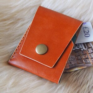 May include: A brown leather wallet with a flap closure and a metal button. The wallet is folded and has a £20 bill sticking out.