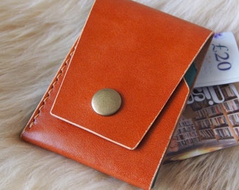 May include: A brown leather wallet with a flap closure and a metal button. The wallet is folded and has a £20 bill sticking out.