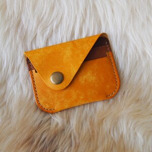 May include: A small, yellow leather wallet with a brown leather flap and a gold snap closure.