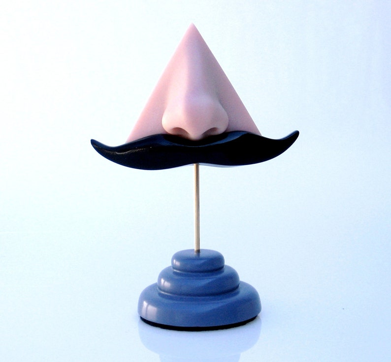 Może przedstawiać: R&oacute;żowy tr&oacute;jkątny nos z czarnym wąsem na niebieskim stojaku.