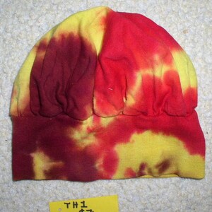 May include: A tie-dye beanie hat in shades of red, yellow, and maroon. The hat has a folded brim and a soft, textured appearance. The tag reads "TH1 $7".