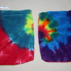 May include: Two tie-dye drawstring pouches. One is predominantly red, blue, and yellow, the other is purple, blue, orange, and yellow. Each pouch has a white drawstring closure at the top.