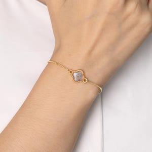 Puede incluir: Un delicado brazalete de cadena dorada con un pequeño dije de trébol de cuatro hojas con una flor prensada en el centro.