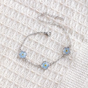 Puede incluir: Un brazalete de cadena de plata con tres delicados encantos con flores de nomeolvides prensadas.