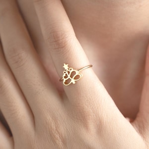 Puede incluir: Un anillo de oro con un delicado diseño de árbol de Navidad recortado. El anillo se lleva en un dedo.