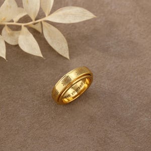 May include: A gold-toned metal ring featuring a rotating outer band engraved with small flower motifs. The inner band of the ring is clearly engraved with the text "believe yourself" in a simple, legible font, visible from the side angle.