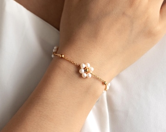 May include: A gold chain bracelet with small white pearls and a flower charm made of pearls. The flower charm has a gold centre.