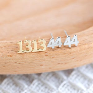 Może przedstawiać: Dwa pary kolczyków z cyframi. Jedna para jest złota i ma napis "1313". Druga para jest srebrna i ma napis "4444".