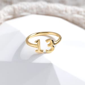 May include: Gold ring featuring the number 13 in a bold, stylised font.