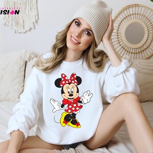 May include: White sweatshirt with a red and black Minnie Mouse graphic. The sweatshirt has a crew neck and long sleeves.