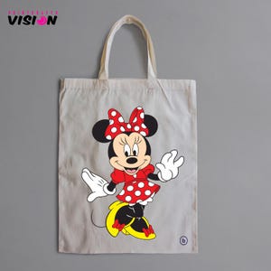 May include: A white canvas tote bag with a red and white polka dot Minnie Mouse design. The bag has black handles and a red bow on Minnie's head.