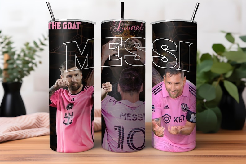 May include: Three stainless steel tumblers with black and white designs featuring a soccer player wearing a pink jersey with the name "Messi" and the number "10" on the back. The tumblers have black backgrounds with white text that reads "Lionel Messi" and "The Goat".