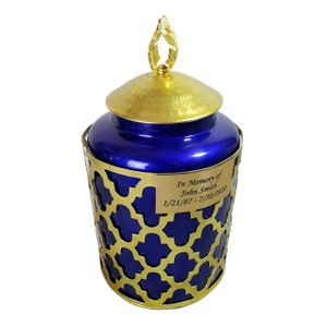 May include: Blue and gold cremation urn with a decorative gold lattice design and a gold lid with a leaf finial. The urn has a personalised plaque that reads "In Memory of John Smith 1/21/87 - 7/30/2020".