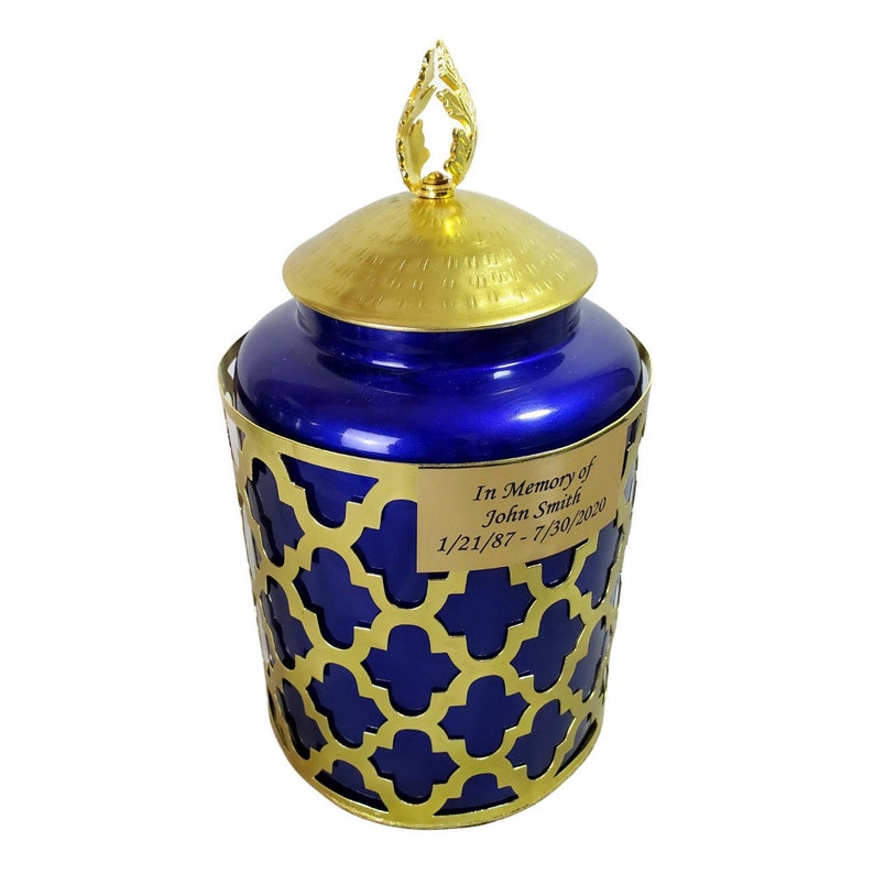 May include: Blue and gold cremation urn with a decorative gold lattice design and a gold lid with a leaf finial. The urn has a personalised plaque that reads "In Memory of John Smith 1/21/87 - 7/30/2020".