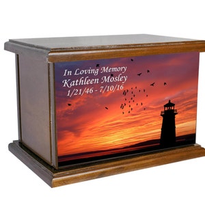 May include: Wooden cremation urn featuring a sunset and lighthouse image. The urn is inscribed with the text "In Loving Memory Kathleen Mosley 1/21/46 - 7/10/16".