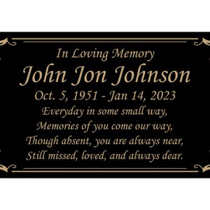 May include: Black memorial plaque with gold lettering. "In Loving Memory John Jon Johnson Oct. 5, 1951 - Jan 14, 2023 Everyday in some small way, Memories of you come our way, Though absent, you are always near, Still missed, loved, and always dear."