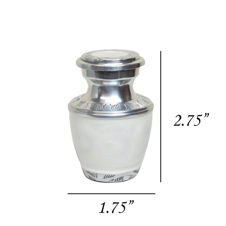 May include: Silver cremation urn with a white finish and engraved details. The urn is 2.75 inches tall and 1.75 inches wide.
