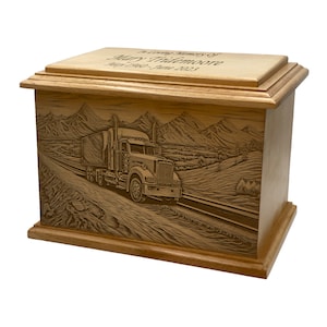 May include: A wooden urn with a detailed engraving of a semi-truck driving on a road through a mountainous landscape. The top of the urn has the inscription "In Loving Memory of Mary Thiemoore, May 1960 - June 2023".