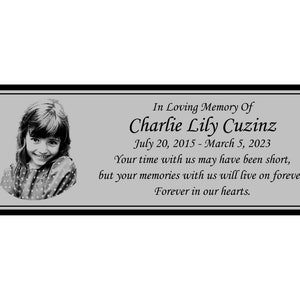 May include: A black and white photo of a young girl is on a silver plaque with the text "In Loving Memory Of Charlie Lily Cuzinz July 20, 2015 - March 5, 2023 Your time with us may have been short, but your memories with us will live on forever. Forever in our hearts."