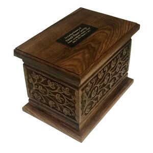 May include: A dark brown wooden cremation urn with an engraved floral design and a brass plaque with the inscription "In loving memory of Donald Grace Sterling, Father, Grandfather, Friend, July 20, 1937 - March 11, 2021".