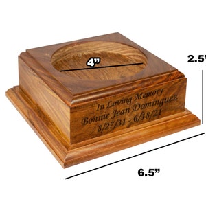 May include: A wooden memorial box with a square base and a circular opening. The box is 6.5 inches long, 4 inches wide, and 2.5 inches tall. The inscription reads "In Loving Memory Bonnie Jean Dominguez 8/27/31 - 6/18/21."