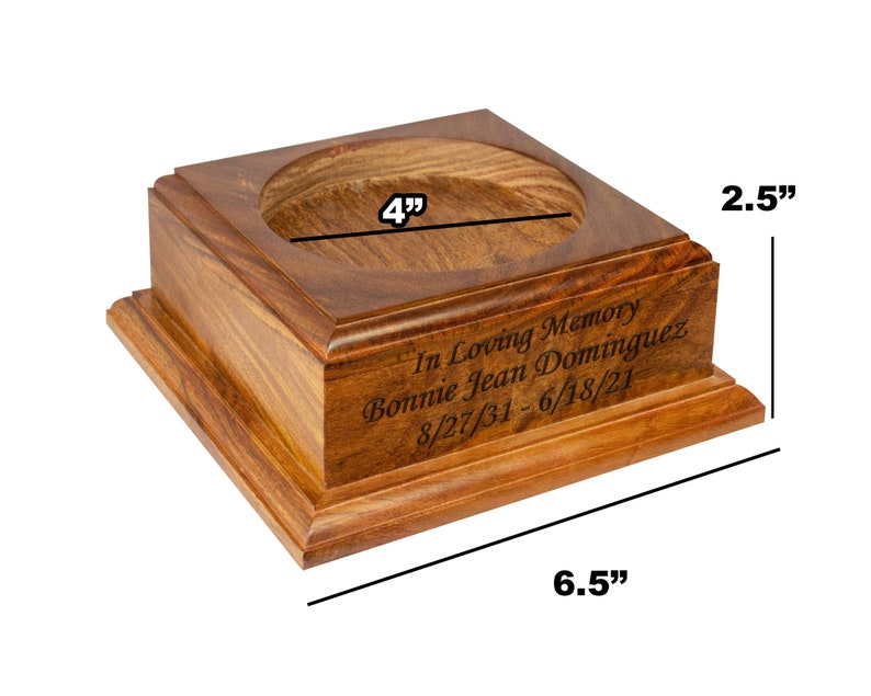 May include: A wooden memorial box with a square base and a circular opening. The box is 6.5 inches long, 4 inches wide, and 2.5 inches tall. The inscription reads "In Loving Memory Bonnie Jean Dominguez 8/27/31 - 6/18/21."
