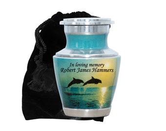 May include: A small teal and silver urn with a sunset and dolphin image. The urn has the inscription "In loving memory Robert James Hammers".