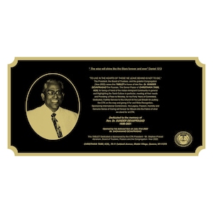 Op de afbeelding: Een gouden plaquette met zwarte letters op een zwarte achtergrond. De plaquette herdenkt het leven van Rev. Dr. Sunder Devaprasad, oprichter van de Christava Tamil Kol, een Tamil-kerk in Queens, New York. De plaquette werd in juli 2022 ingehuldigd.