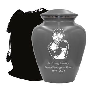 May include: Gray metal urn with a white silhouette of a football player holding a football. The urn has the text "In Loving Memory James Dominguez Dean 1975 - 2024" engraved on the front.