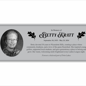 Peut inclure: Plaque commémorative grise avec un portrait de Betty Kratt. Le texte indique "À la mémoire de Betty Kratt, 30 septembre 1935 - 25 mai 2024." Le texte supplémentaire détaille ses contributions à Wyandotte Hills et à la communauté.