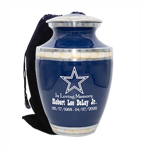 May include: A blue and silver cremation urn with a white star and the inscription "In Loving Memory Robert Lee DeLay Jr. 06/17/1968-04/07/2020".