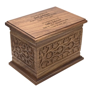May include: A wooden cremation urn with an intricate carved floral design. The lid is engraved with the names "Jack Johnson" and "Sally Johnson" along with their birth and death dates. The inscription reads "In Loving Memory of... Until we meet again..."