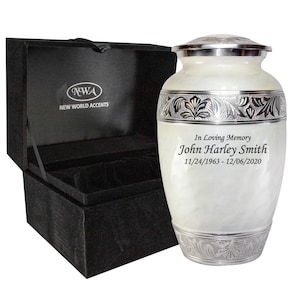 May include: White cremation urn with silver accents and engraved inscription "In Loving Memory John Harley Smith 11/24/1963 - 12/06/2020". The urn comes in a black velvet box with the NWA logo.